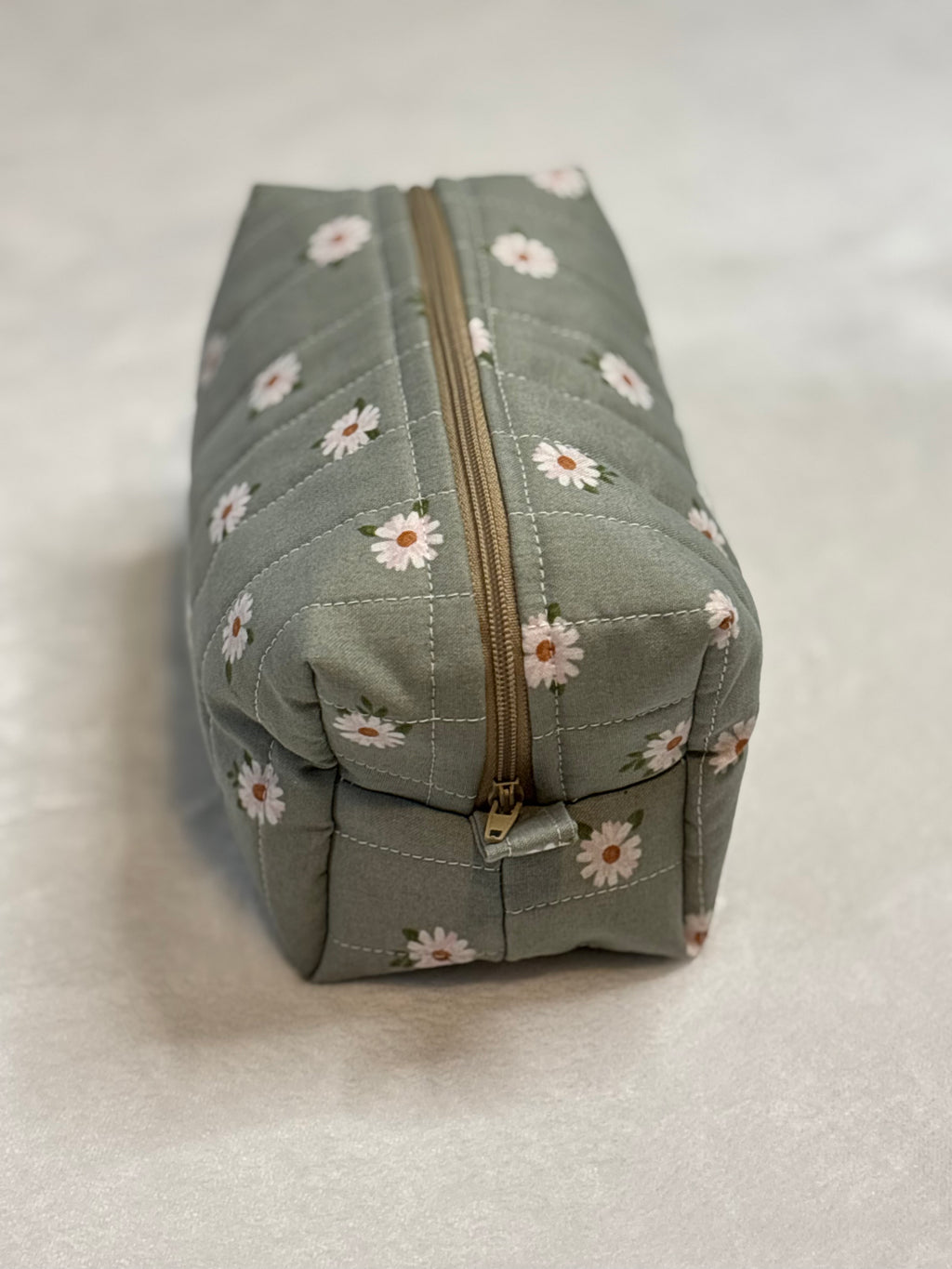 Side view of small quilted Lazy Daisy makeup bag showing warm tan zipper