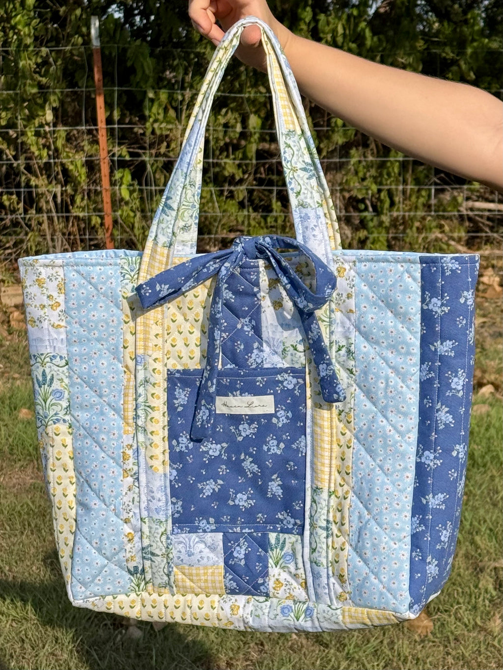 Something Blue Purse held up showing quilted patchwork exterior with navy bow closure and front pocket